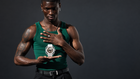 A man in a green tank top holds a white Casio watch in his hands against a dark gray studio background.