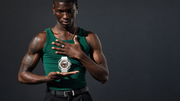 A man in a green tank top holds a white Casio watch in his hands against a dark gray studio background.